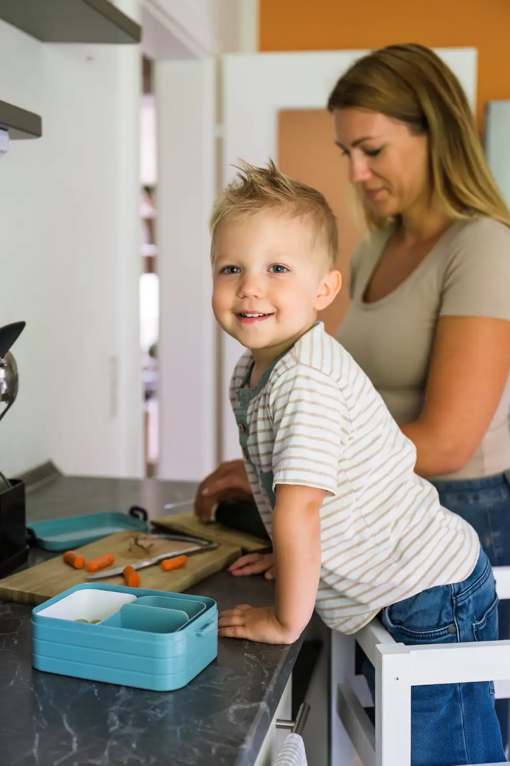a boy leaning on a countertop enjoying family time in the kitchen.